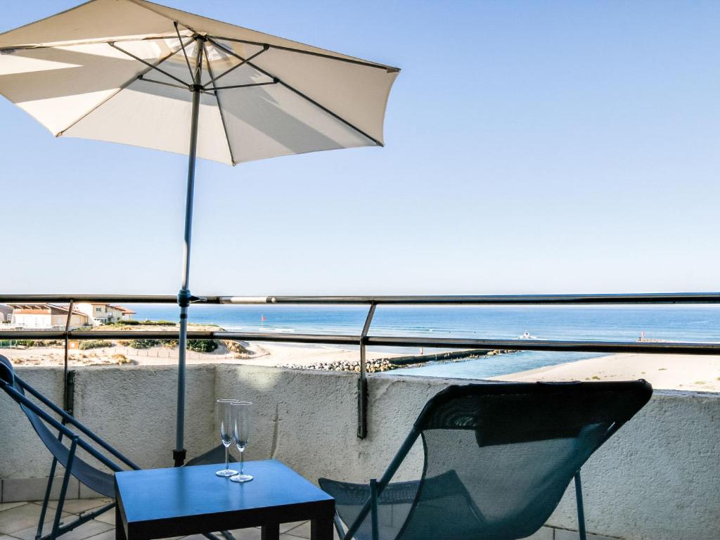 a table and two chairs and an umbrella on a balcony at Apartment Grand Pavois-2 by Interhome in Mimizan-Plage