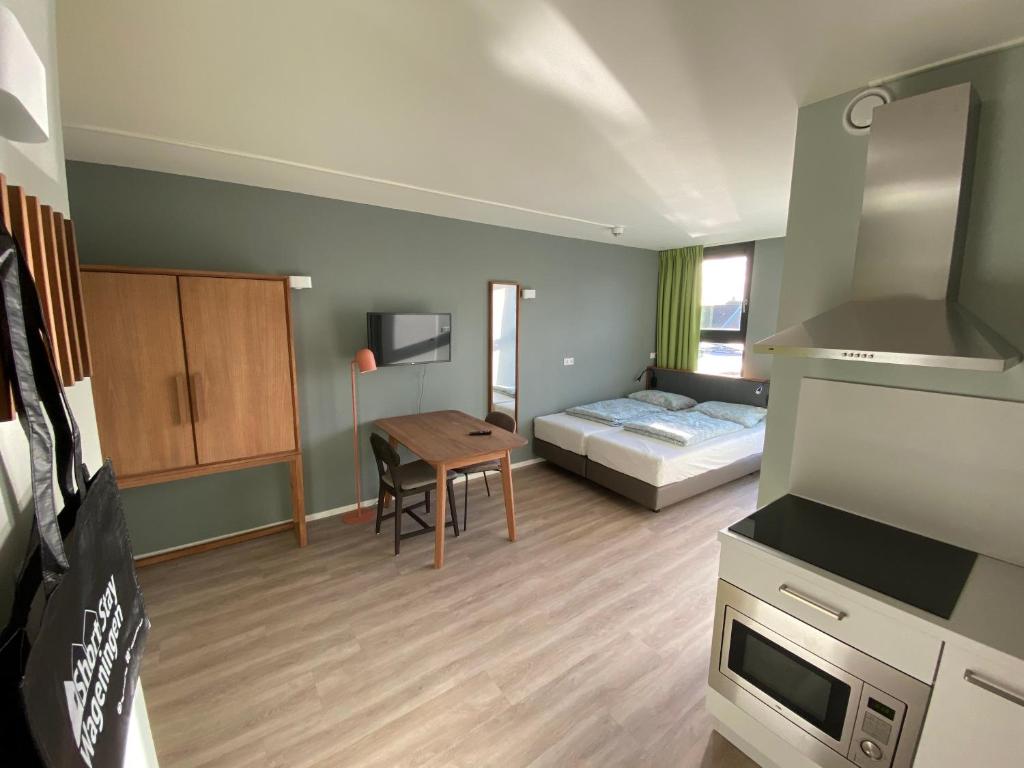 a small room with a bed and a table and a kitchen at Short Stay Wageningen in Wageningen
