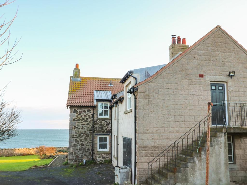 an old stone house with the ocean in the background at The Rest in Eyemouth