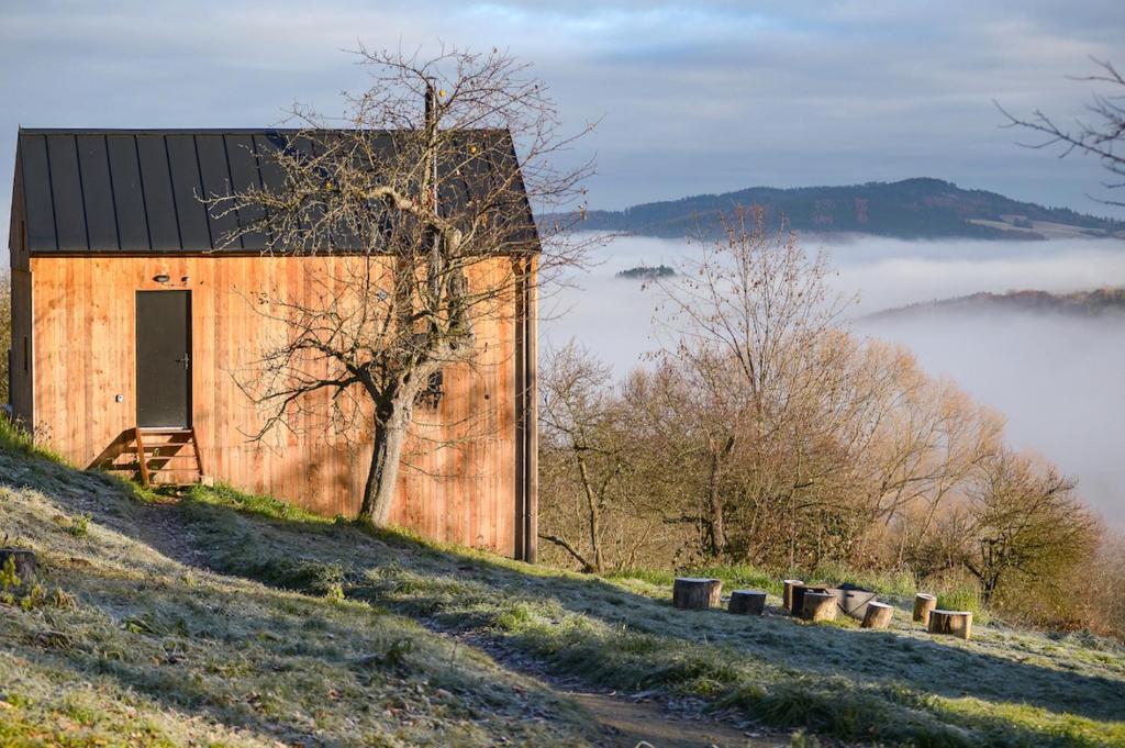 a large wooden barn on a hill with fog in the background at Tři domky in Děpoltice