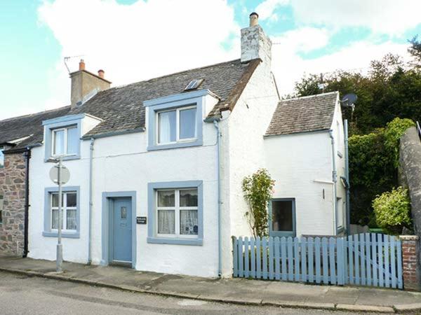 a white house with a blue fence on a street at Nathaniel's Cottage in Kirkcudbright