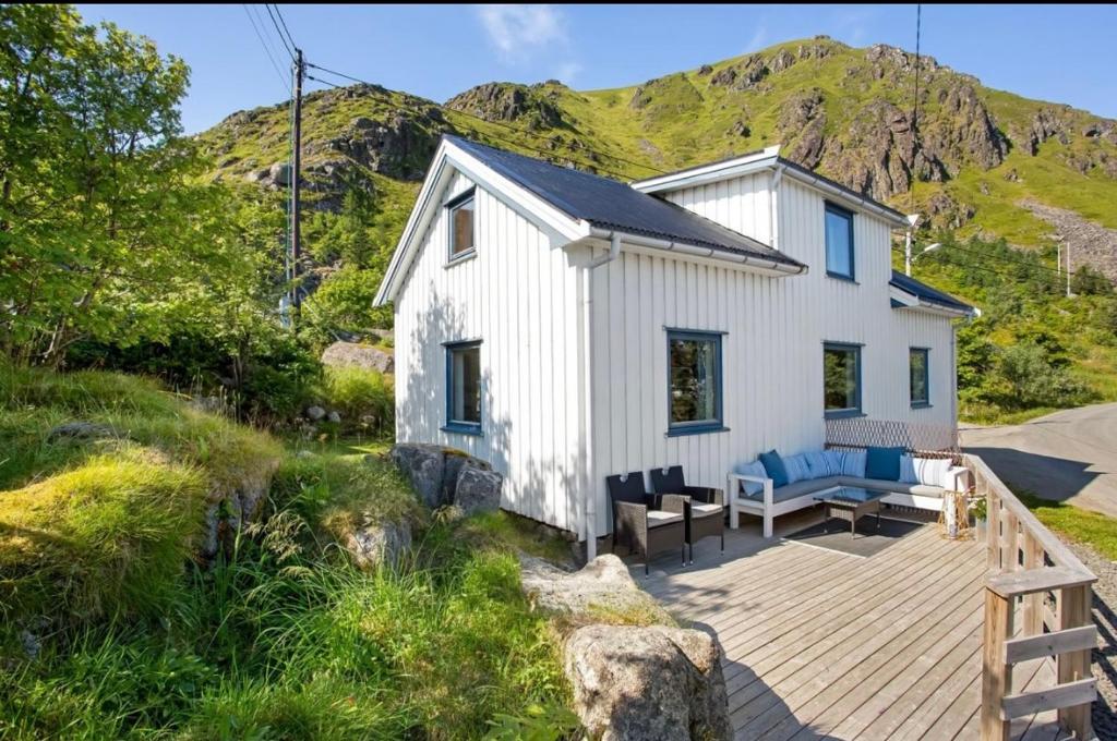 a white cottage with a deck and mountains in the background at Kræmmervikveien 33 in Ballstad