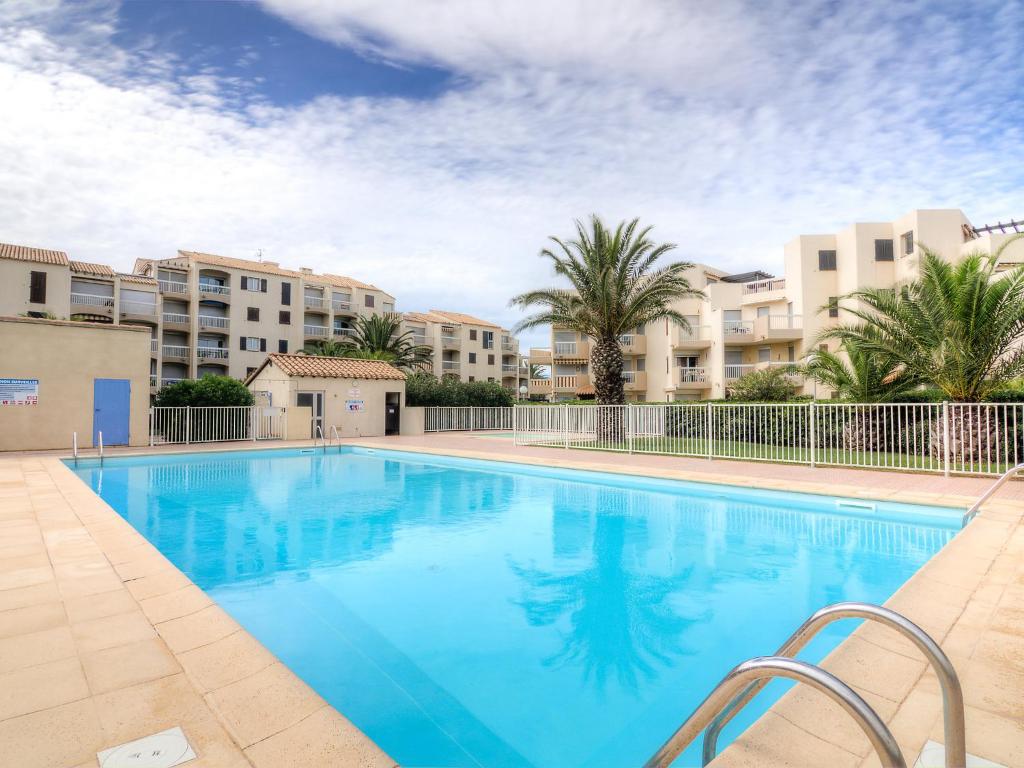 une grande piscine avec des palmiers et des bâtiments dans l'établissement Apartment Les Frégates-13 by Interhome, à Saint Cyprien Plage