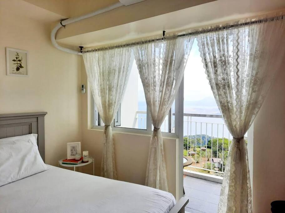 a bedroom with a bed and a large window at 1 BR Cozy Farmhouse-Style Condo with Balcony & Taal View at Wind Residences in Tagaytay
