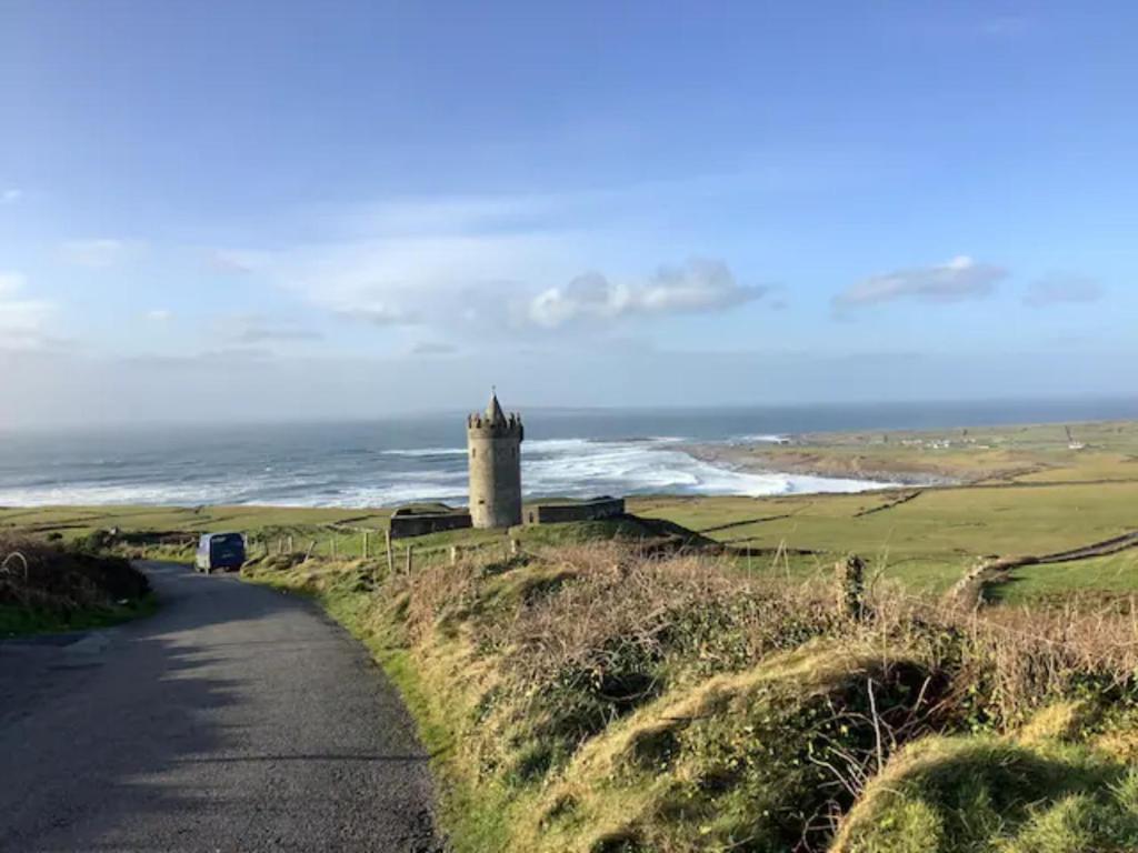 a road leading to a castle on a hill next to the ocean at Hardy’s Cottage in Doolin