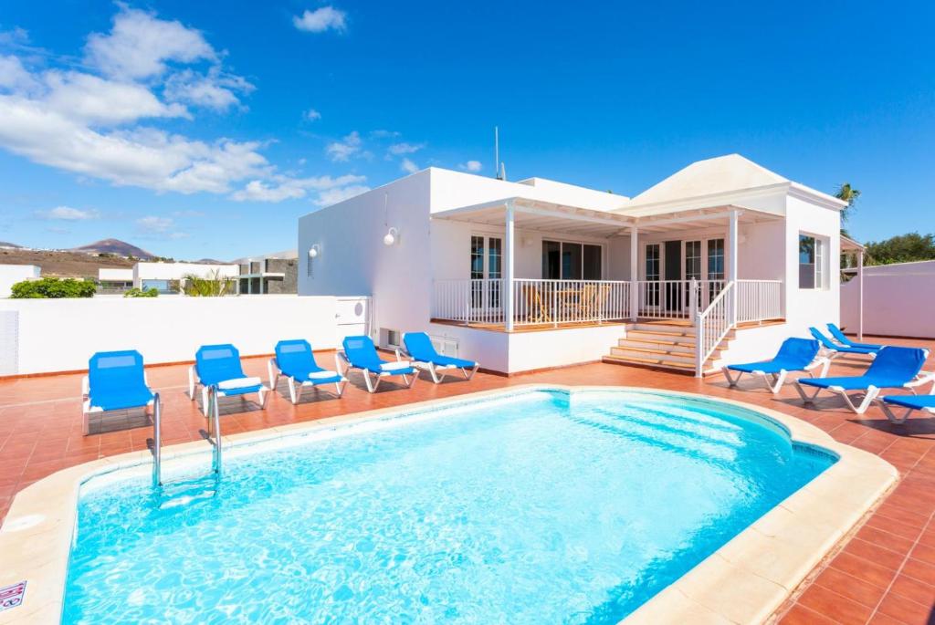 ein Pool mit blauen Stühlen und ein Haus in der Unterkunft Villa Candela in Puerto del Carmen