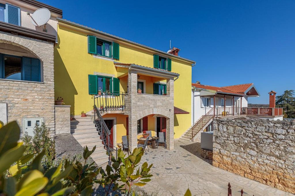 Casa amarilla con persianas verdes y pared de piedra. en Apartments Grgeta Funtana, en Funtana
