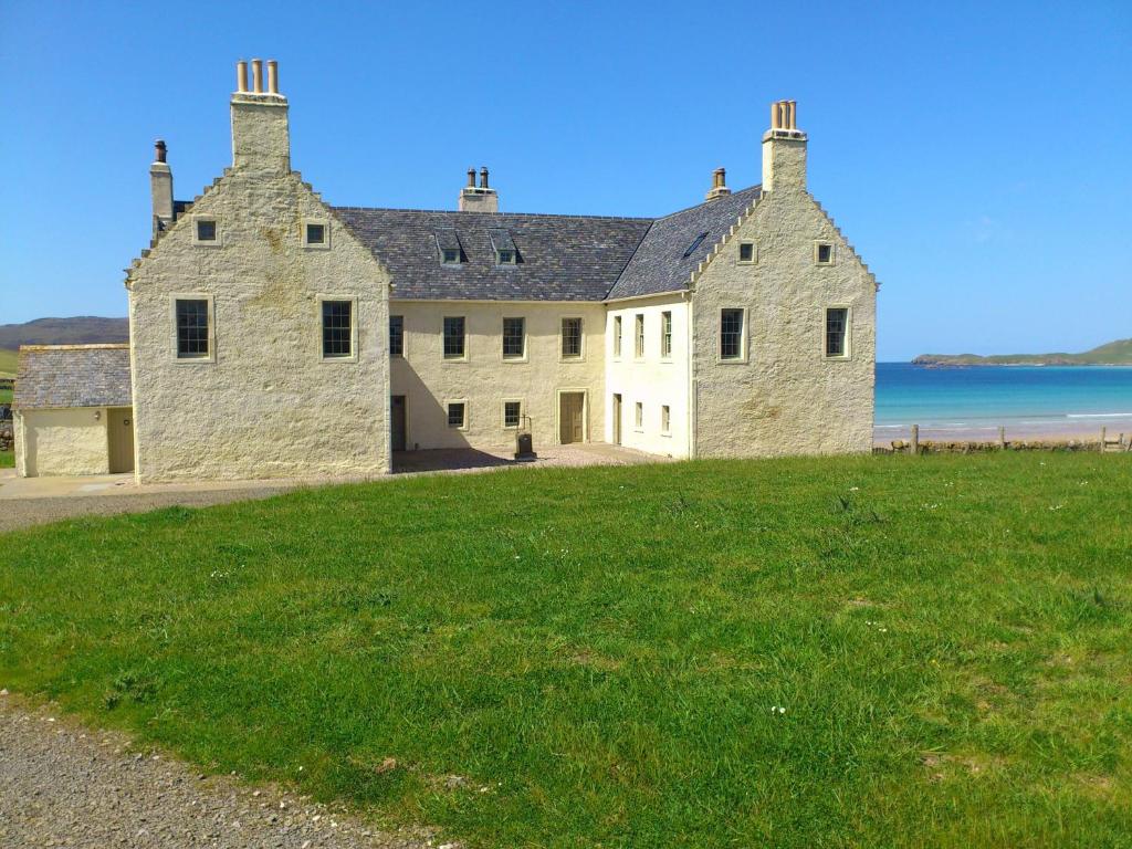 a large stone building on the side of a grass field at Balnakeil House in Balnakeil