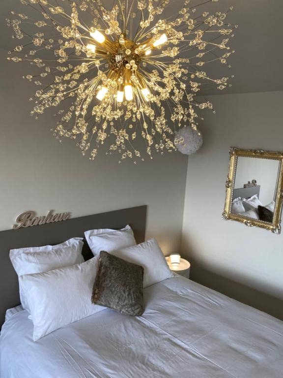 a large chandelier above a bed with white pillows at Cocon déco + terrasse & parking fermé Zénith Ester in Limoges