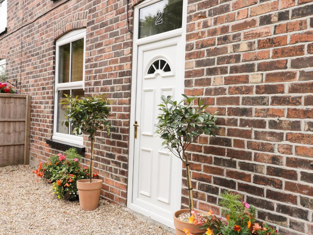 uma casa de tijolos com uma porta branca e vasos de plantas em 2 Moor Farm Cottages em Flinton