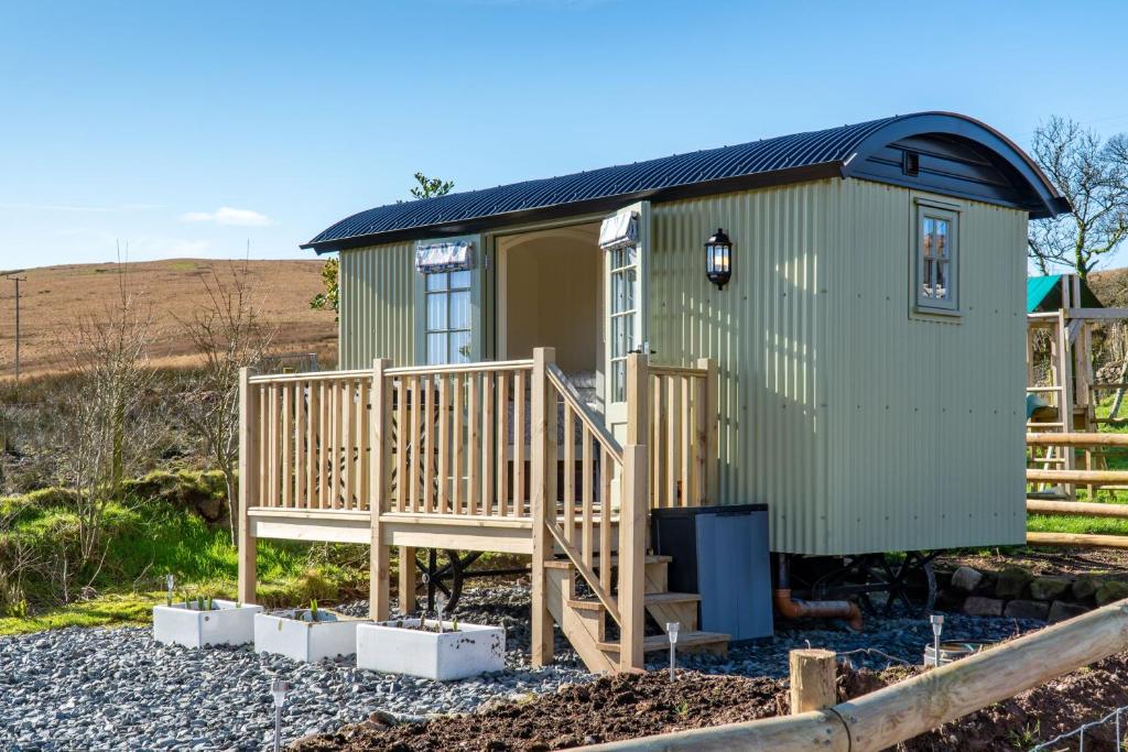 a green tiny house with a porch and a deck at Scalderskew Shepherds Hut in Gosforth