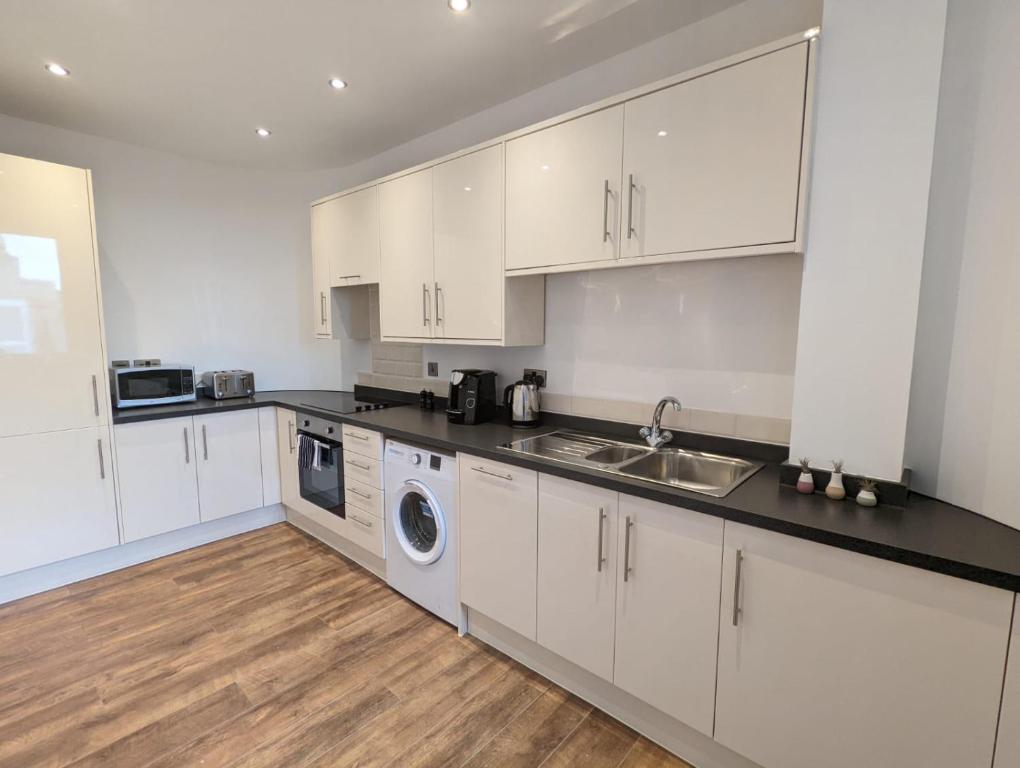 a kitchen with white cabinets and a sink and a dishwasher at Swindon Apartments by Charles Hope in Swindon