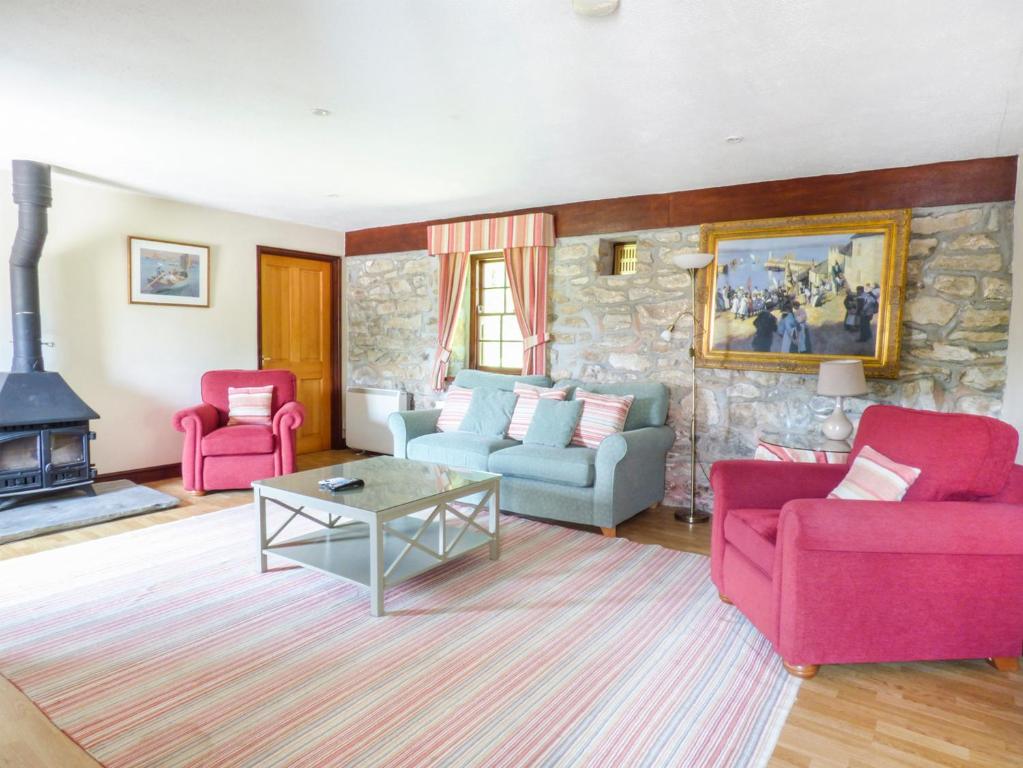 a living room with two pink chairs and a stone wall at Flower House in Saint Erth