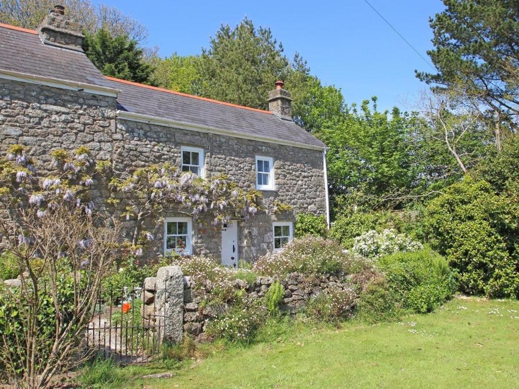 an old stone house with flowers in front of it at Woodpecker Cottage in Helston