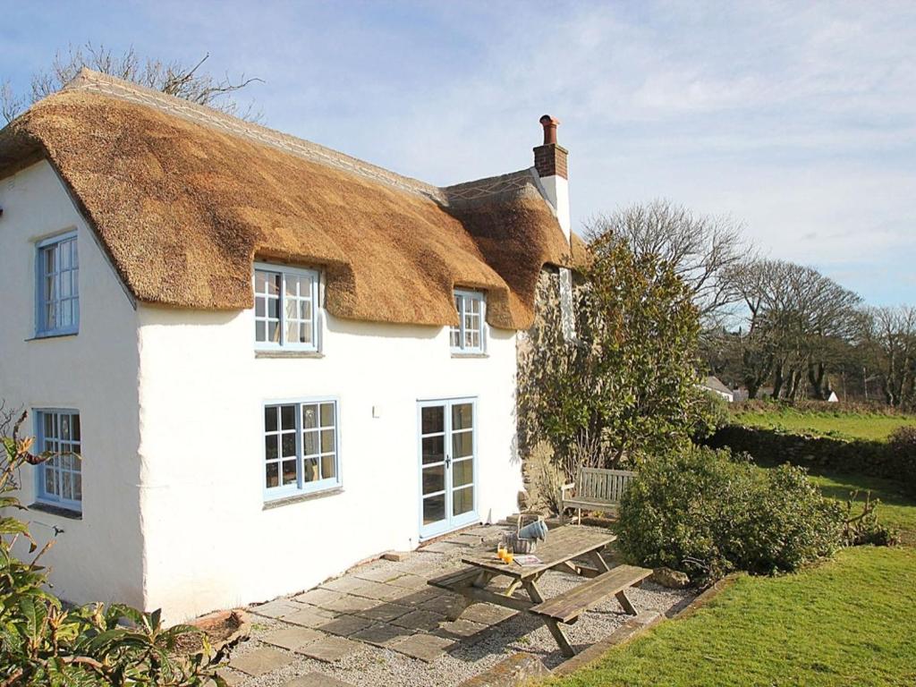 a white house with a thatched roof and a picnic table at Rose Cottage in Helston