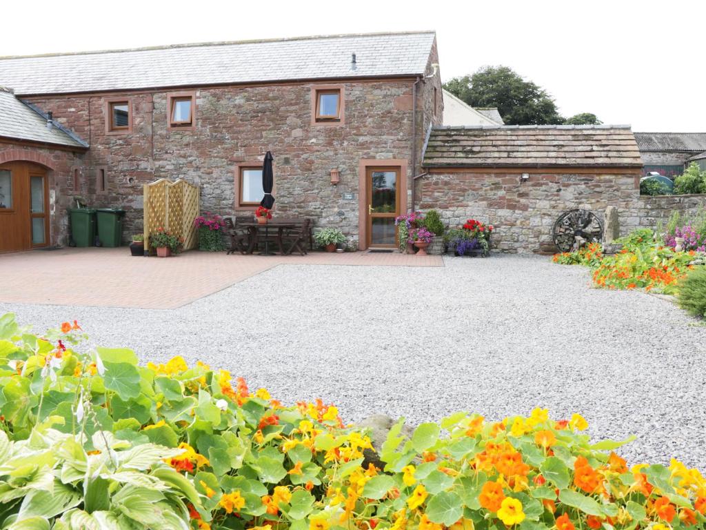 a stone house with a patio and flowers at Piggery Cottage in Wigton