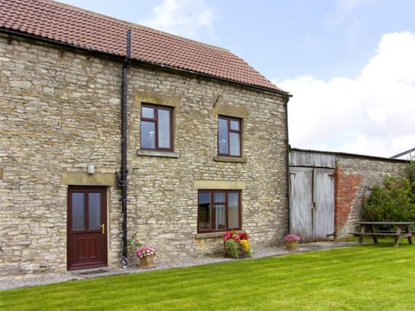 uma casa de tijolos com um relvado verde em frente em Wethercote Cottage em Cold Kirby