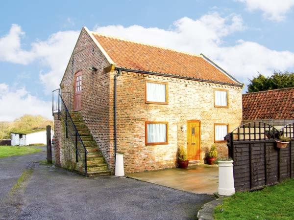 a brick house with a yellow door and a gate at Croft Granary in Stillington