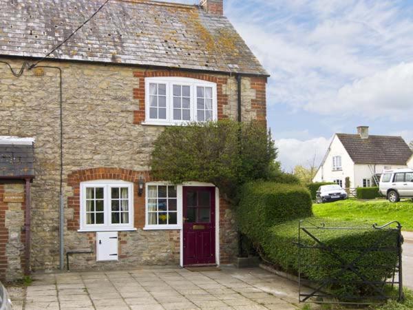 ein Backsteinhaus mit einer roten Tür und weißen Fenstern in der Unterkunft Candy Cottage in Bradford Abbas