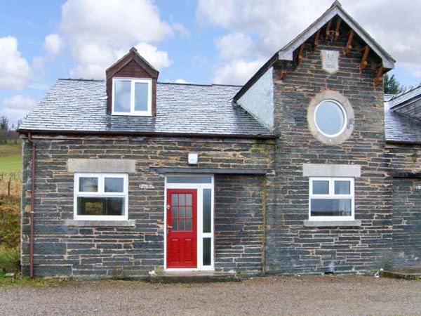 une petite maison en briques avec une porte rouge dans l'établissement Hendre Aled Cottage 3, à Llansannan