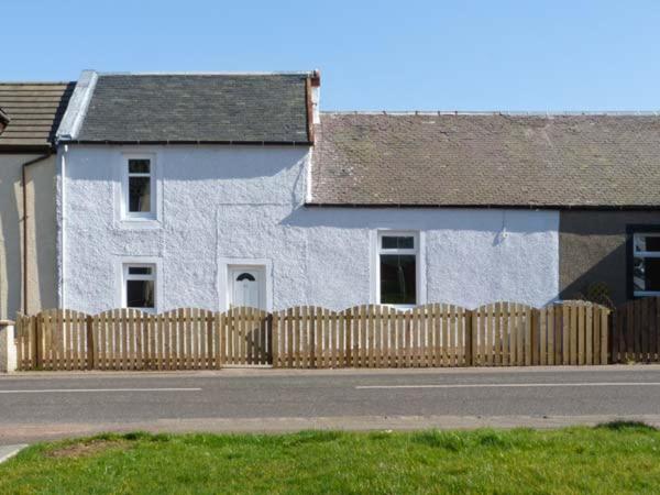 a white house with a wooden fence in front of it at Sky Blue Cottage in Forth