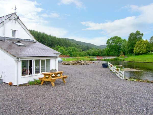 a building with a picnic table next to a river at Harrison's Cottage in Llandegla