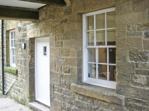 a stone house with a white door and a window at No 5 The Stables in Pateley Bridge