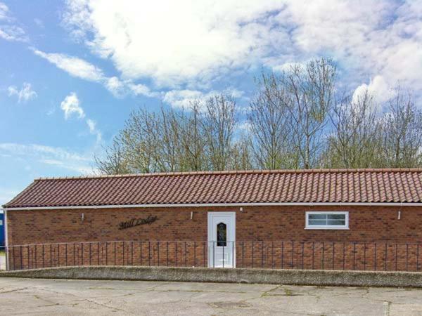 a brick building with a white door and a red roof at Mill Lodge in Brisley
