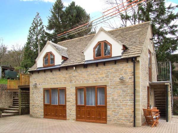 una pequeña casa de ladrillo con puertas de madera marrón en Rowan Studio, en Great Witcombe