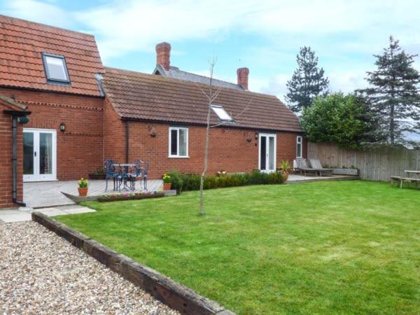 a red brick house with a yard with a green lawn at The Barn Ivy Cottage in Dunnington