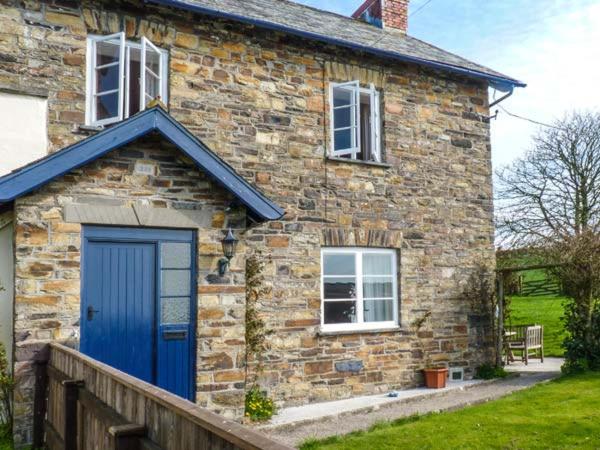 una casa de ladrillo con una puerta y ventanas azules en Buckinghams Leary Farm Cottage, en Filleigh