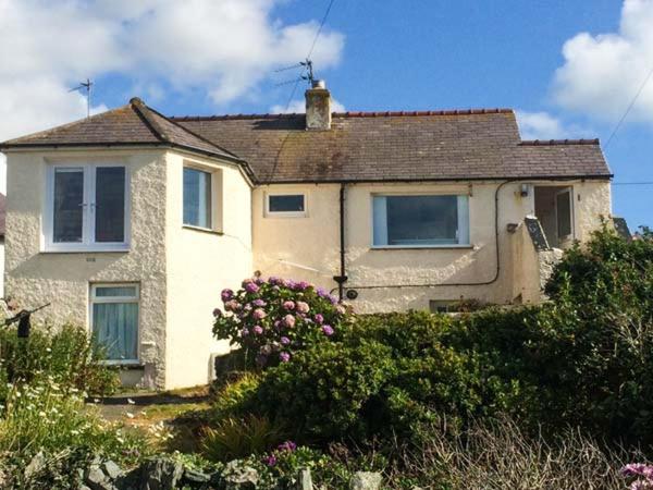 a white house with flowers in front of it at Ty'r Enfys Bach - Upper in Trearddur