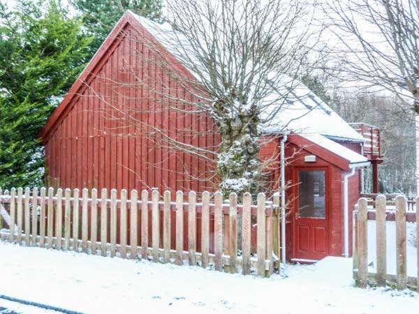 a red barn with a fence in the snow at Strathavon Chalet in Aviemore