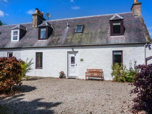 Uma casa branca com um banco à frente. em Deskford Cottage em Balblair