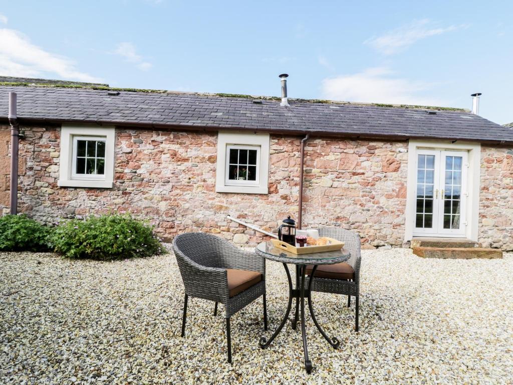 Faraway Cottage في Kirklinton: طاولة وكراسي أمام منزل من الطوب