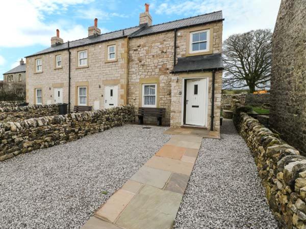 a stone house with a white door and a stone wall at 1 Primitive Croft in Chelmorton