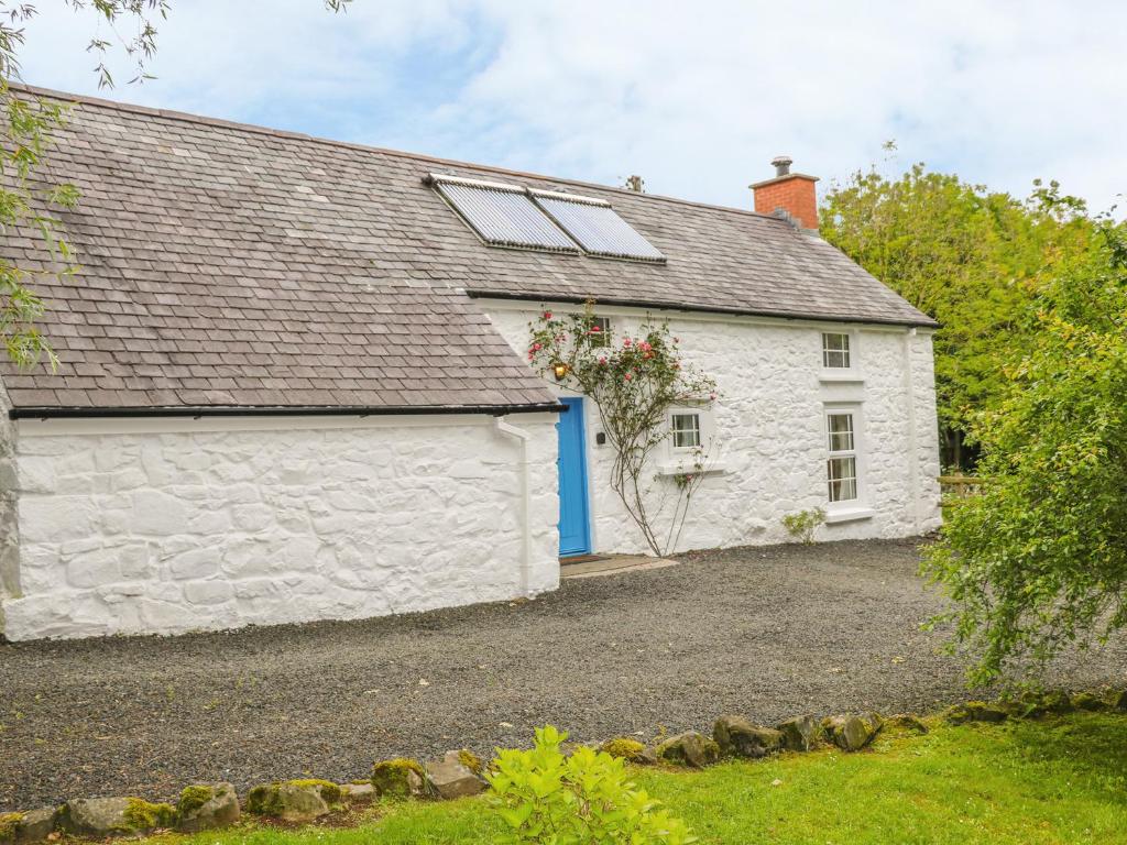 a white cottage with a blue door at Rosslare Cottage in Broughshane
