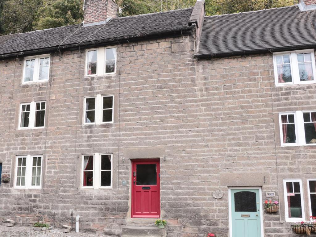 a brick building with a red door and windows at Holly Cottage in Matlock