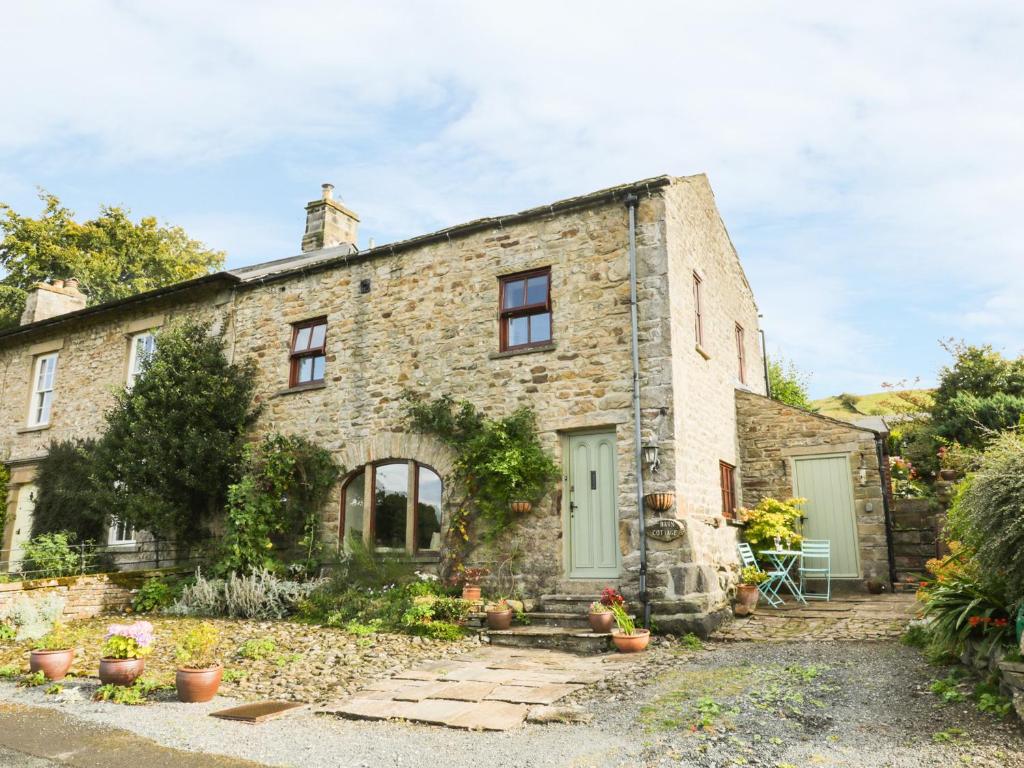 an old stone house with green doors and plants at Barn Cottage in West Burton