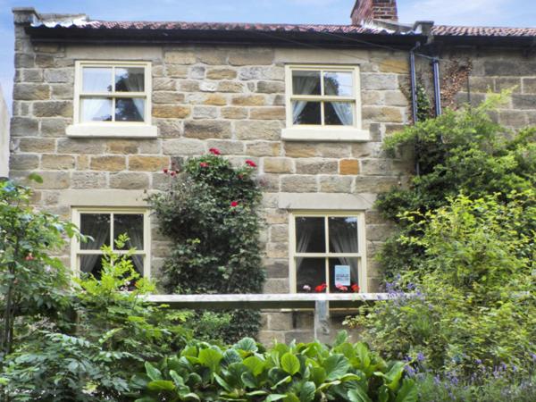a stone house with three windows and bushes at River Cottage in Staithes