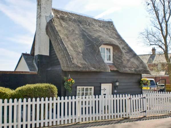 uma casa preta com um telhado de palha e uma cerca branca em Little Thatch em Walton-on-the-Naze