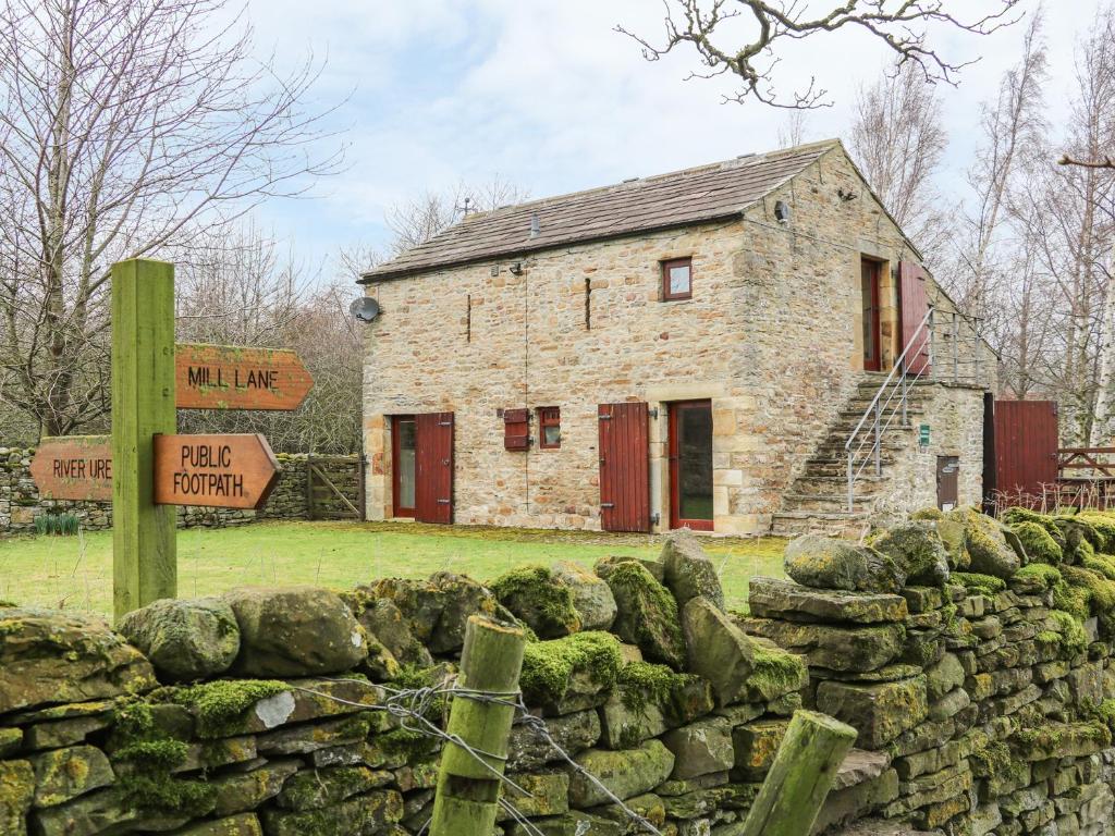 une maison en pierre avec un mur en pierre et un panneau dans l'établissement The Bothy, à Leyburn