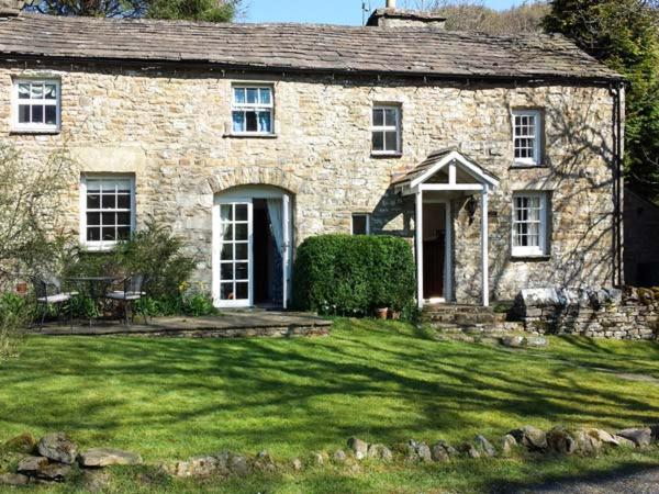 an old stone house with a green lawn in front of it at Farrier's Cottage in Sedbergh