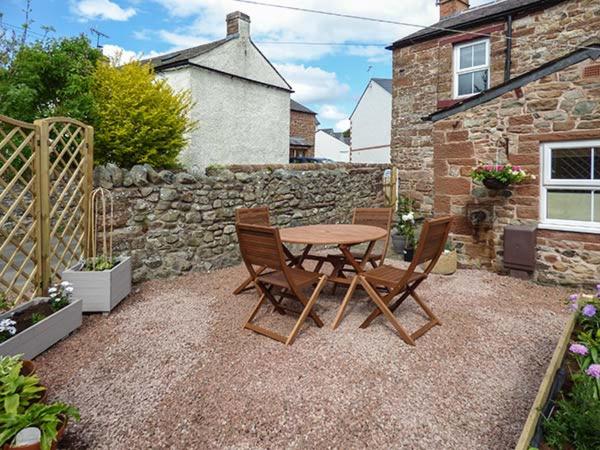 a patio with a table and chairs and a stone wall at Bakers Cottage in Newbiggin