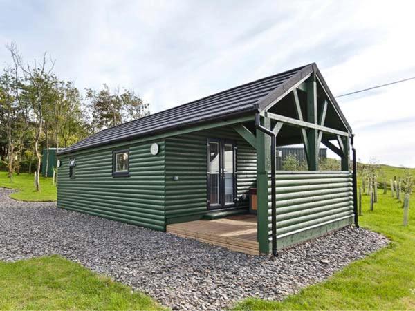 a green cabin with a porch on a field at Ash Lodge in Ulverston