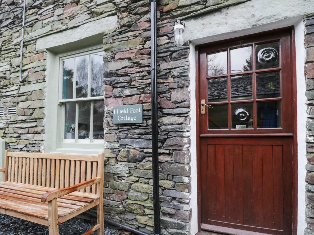 eine Holzbank neben einem Steingebäude mit einer Tür in der Unterkunft 1 Field Foot Cottage in Ambleside