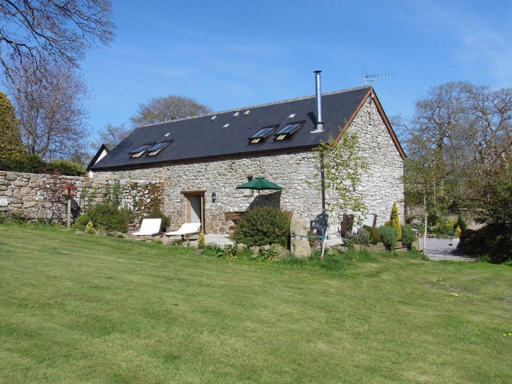 a stone house with a black roof and a yard at Butterdon Barn in Moretonhampstead