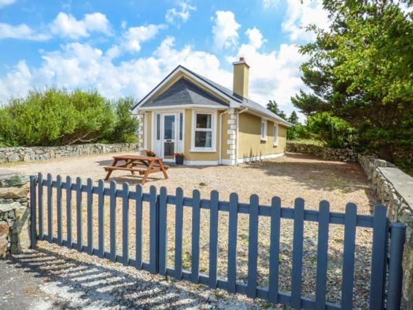 ein kleines gelbes Haus mit einem Picknicktisch und einem Zaun in der Unterkunft Ti Sheamuis in Clifden