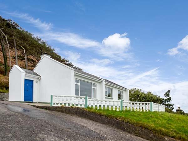 una casa blanca con una valla al lado de una carretera en Rossbeigh Beach Cottage No 6, en Rossbeigh