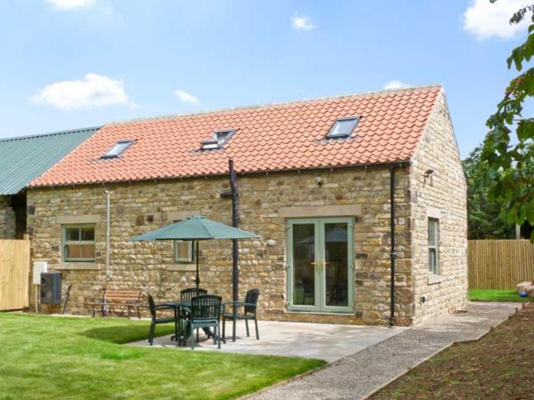 a stone house with a table and chairs and an umbrella at Summer Farm Cottage in Bedale